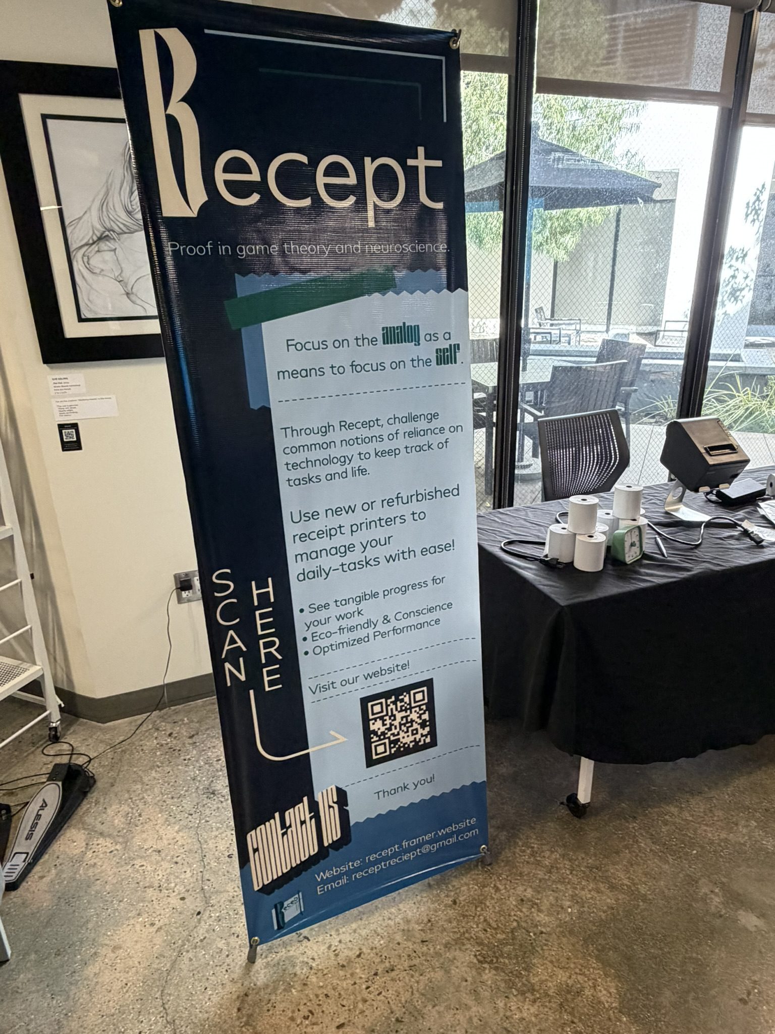 Tall blue exhibition banner with 'Receipt' branding and a QR code near the bottom; text panels describe project goals and features, set up at a table with a printer and cups nearby.