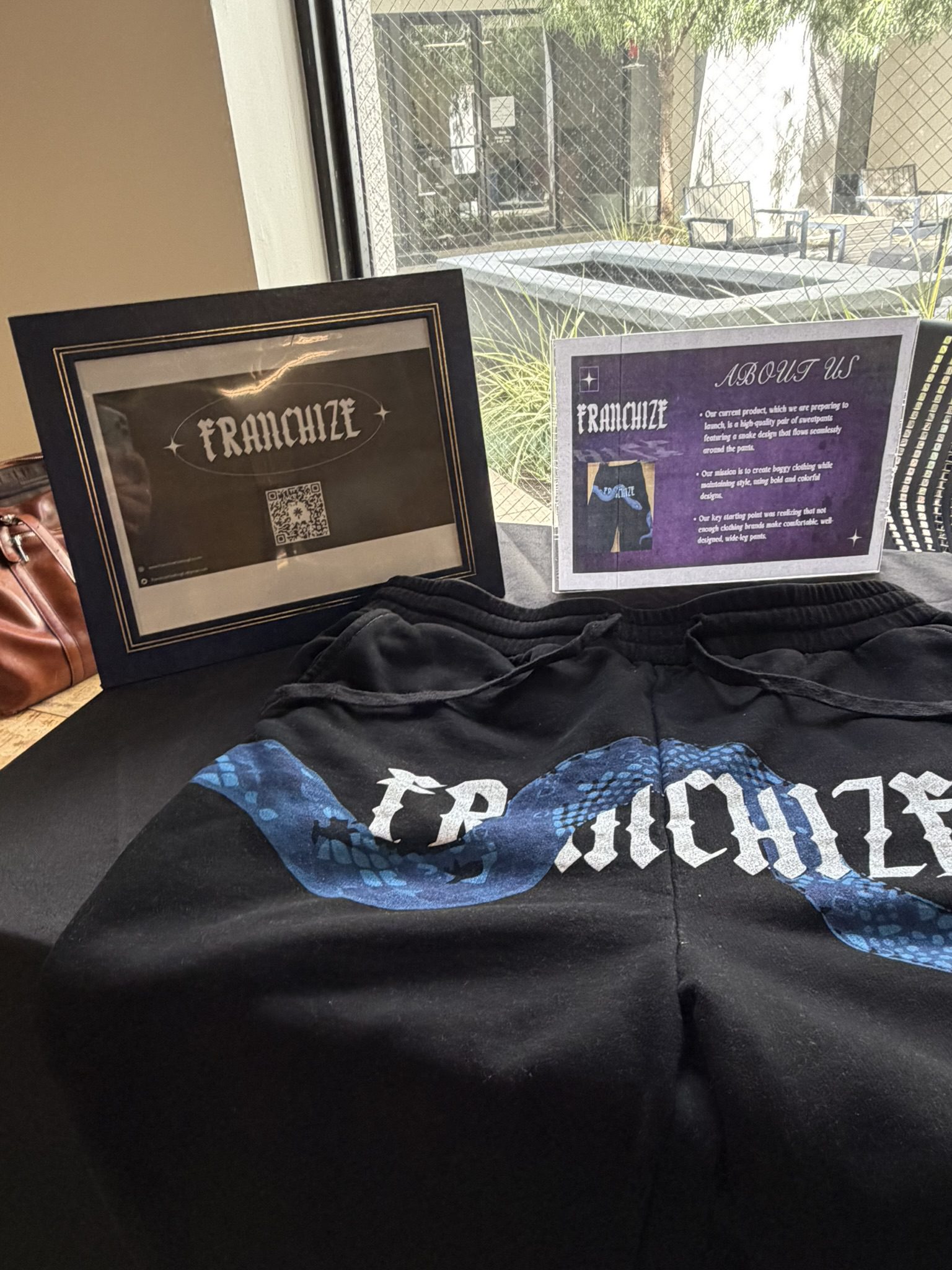Franchise-themed display on a couch with two framed posters and a purple About Us panel containing text and images.